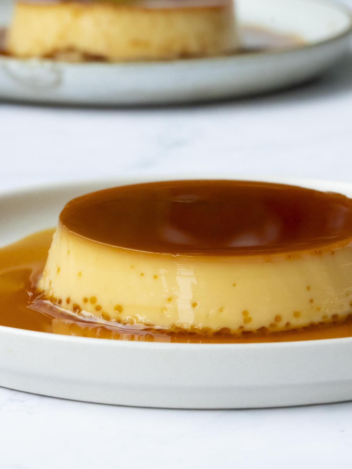 a creamy condensed milk flan put on a white plate and covered in sweet caramelized sugar