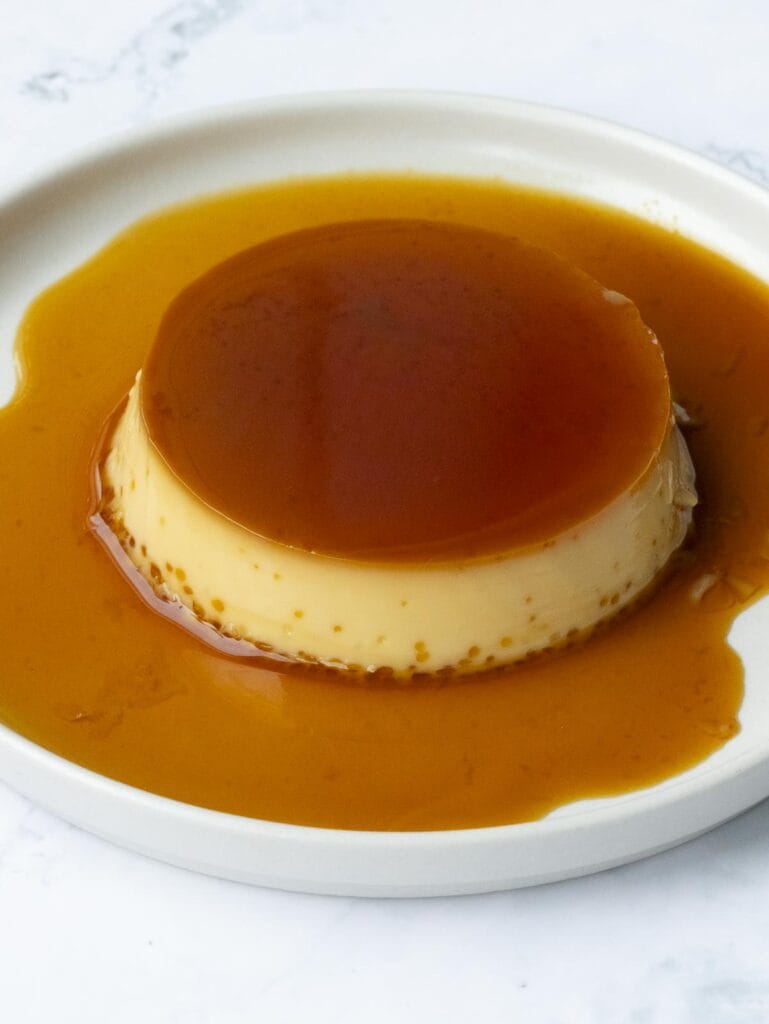 a whole caramel flan put on a white plate and covered in caramel sauce