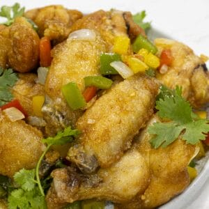 a dish of chinese salt and pepper chicken wings with chopped bell peppers and cilantro as garnish