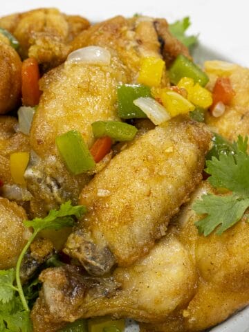 a dish of chinese salt and pepper chicken wings with chopped bell peppers and cilantro as garnish